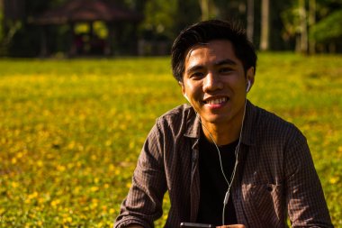 Genç Malay adam onun smartphone Park'taki kullanarak müzik dinlemek zevk