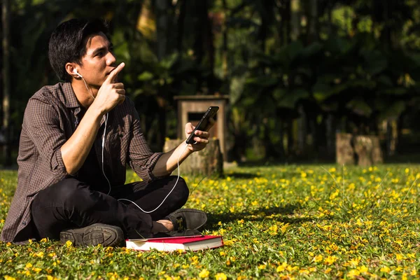 Genç Malay adam onun smartphone Park'taki kullanarak müzik dinlemek zevk