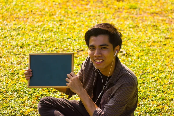 Smiling Young Malay man holding mini blackboard in park