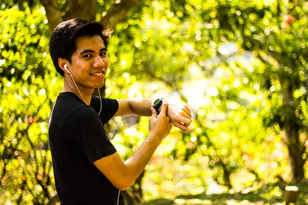 Smiling Young Malay man using watch before jogging in park