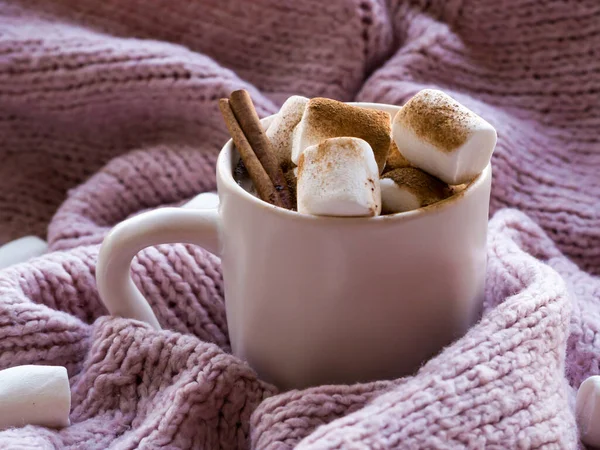 Gemütlichkeit, Stimmung, Lebensstil, Stilllebenskonzept. Becher aromatischer Kakaokaffee mit Marshmallows, Pullover und Zimt auf rosa Strickpullovern als Hintergrund. Traditionelles Winter- oder Herbstheißgetränk zu Hause. — Stockfoto