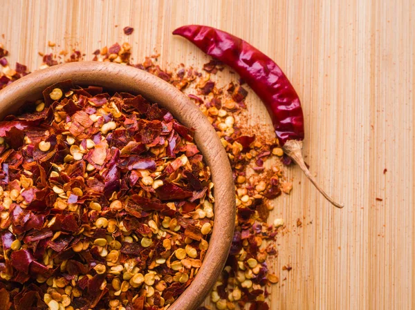 Dried chili pepper flakes in wooden bowl on the wooden table. Dried and crushed fruits of Capsicum frutescens, used as hot spice and for tabasco sauce. Isolated macro food photo close up