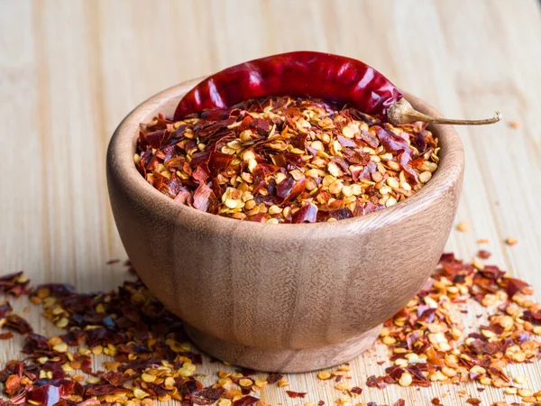 Dried chili pepper flakes in wooden bowl on the wooden table. Dried and crushed fruits of Capsicum frutescens, used as hot spice and for tabasco sauce. Isolated macro food photo close up