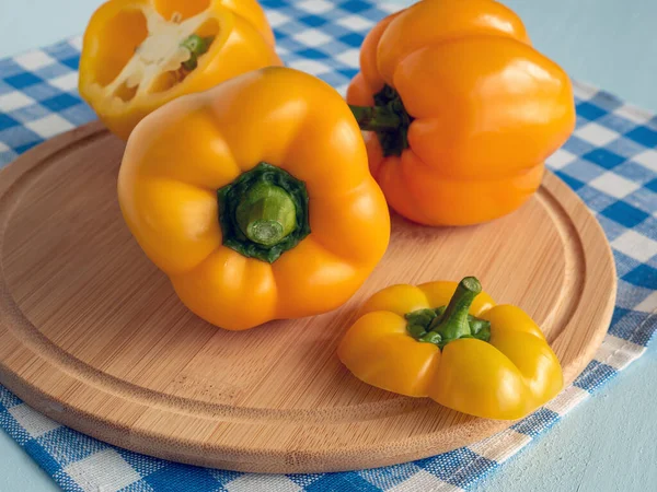 Colorful yellow peppers on cutting board and blue and white linen towel on rustic wooden table. Fresh sweet bell pepper. Colorful and stylish composition. Vegetarian healthy food.