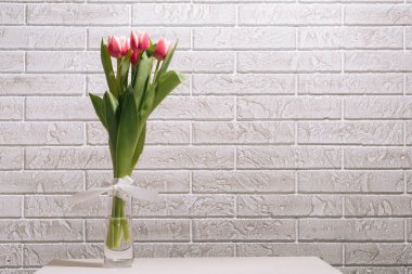 Pembe lale buketi temiz bir vazoda, beyaz tuğladan bir arka planda..