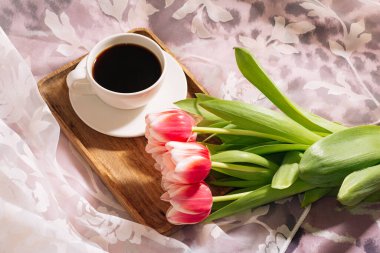 Bir fincan taze kokulu kahve ve ahşap tepside taze pembe laleler..