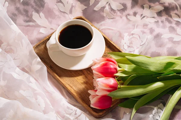 Filiżanka gorącej i aromatycznej świeżo mielonej kawy ze świeżym bukietem biało-różowych tulipanów na drewnianej tacy. Widok z góry — Zdjęcie stockowe