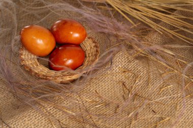Üç tane turuncu tavuklu Paskalya yumurtası, hasır bir sepete boyanmış soğan kabukları, kırsal tarzda kahverengi bir bez üzerinde. Üst görünüm