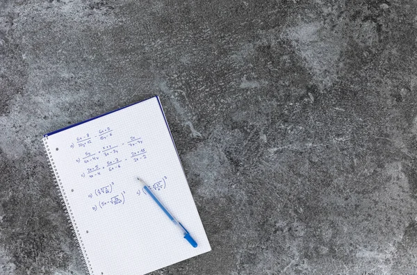 Hand written mathematics book with arithmetic problems, with blue pencil on the book