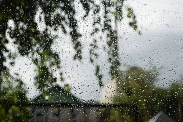 Raindrops on the window pane. Blurred background outside the window in the rain.