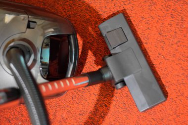 Elinde fırça ve çanta olan bir elektrikli süpürge. Kırmızı halıda elektrikli süpürge..