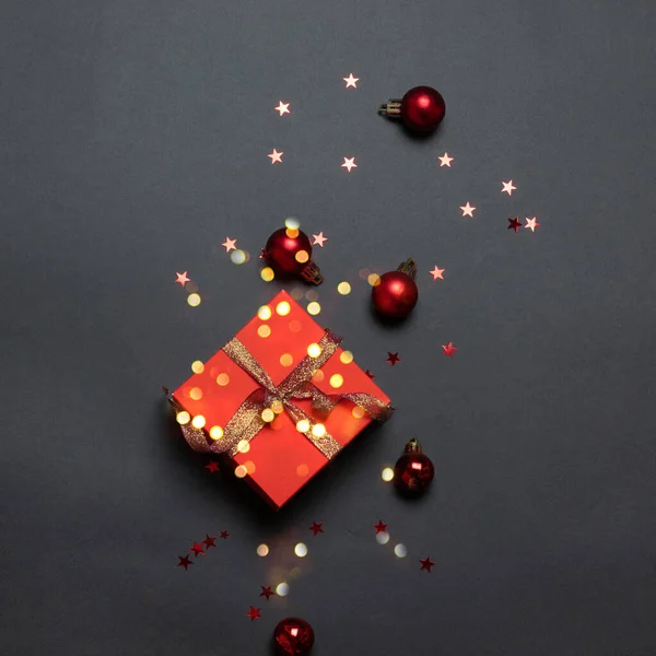 Karácsonyi dekoratív kompozíció piros papír ajándék doboz és arany szalag íj sötét háttér. — Stock Fotó