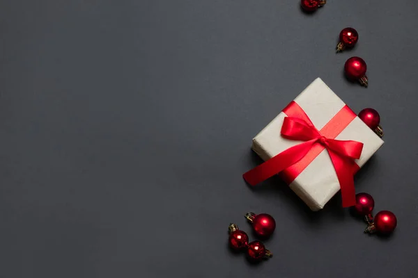 Feliz Navidad y Año Nuevo tarjeta de felicitación con caja de regalo envuelta en papel artesanal con cinta roja y bolas sobre fondo rojo. Vista superior con espacio de copia . —  Fotos de Stock
