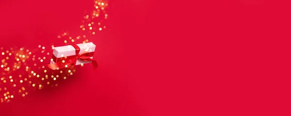 Stor presentförpackning insvept i inslagning rosa papper och en röd satinband rosett flyger i luften på en röd bakgrund med kopia utrymme. — Stockfoto