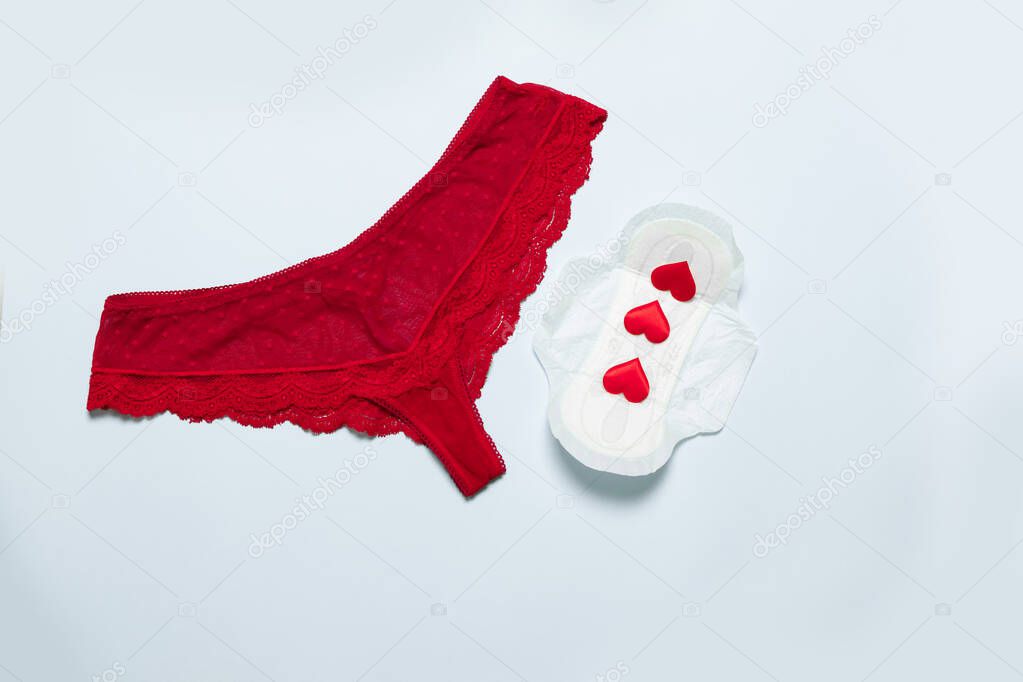 Female lace red panties with medical female slim cotton menstruation pad and love shape against critical days on a blue background. Menstruation, protective equipment.