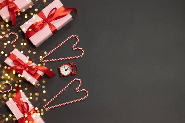 Karácsonyi összetétele ajándékdobozok piros szalagok dekoráció, cukornád, óra és arany csillogó cukorka sötét alapon — Stock Fotó