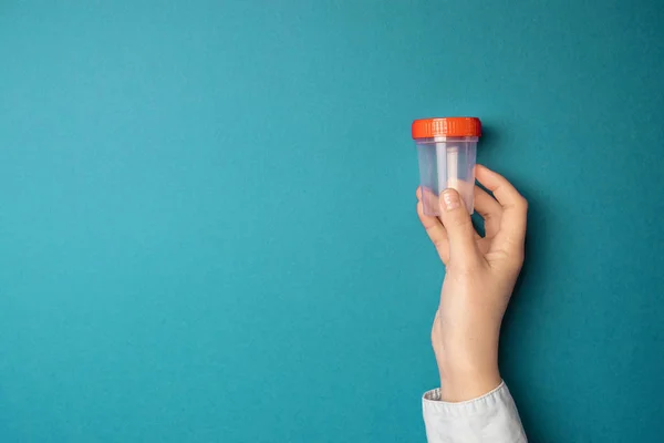 Médico mano en guante médico de látex sostiene un recipiente de plástico con pruebas sobre un fondo azul con espacio de copia — Foto de Stock