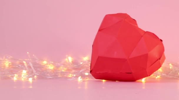 Papier geometrische 3D-Herzform mit goldenen Lichtergirlanden auf rosa Hintergrund. — Stockvideo