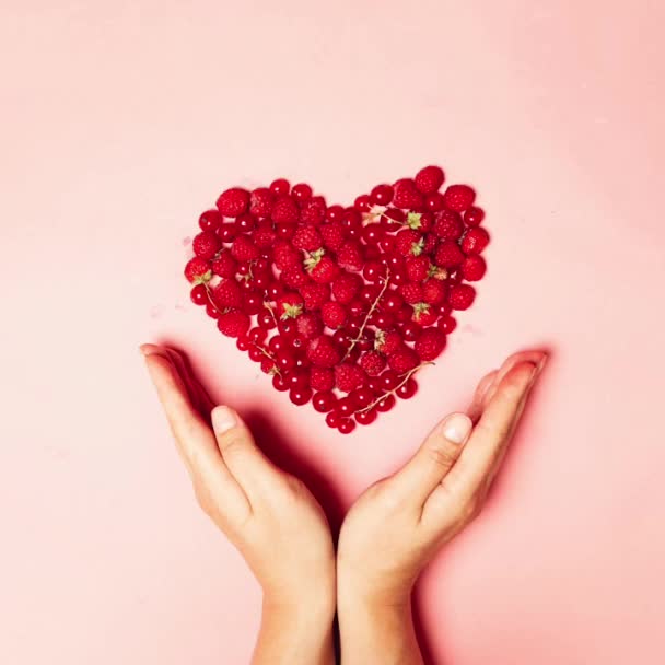 Liebesform aus roten Johannisbeeren, Erdbeeren, Erdbeeren, Kirschen und weiblichen Händen auf rosa Hintergrund. Minimale Komposition mit der Inschrift Sommer — Stockvideo