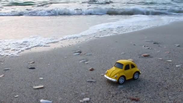 Reizen en vakantie. Speelgoed gele auto op het strand tegen de zee. — Stockvideo