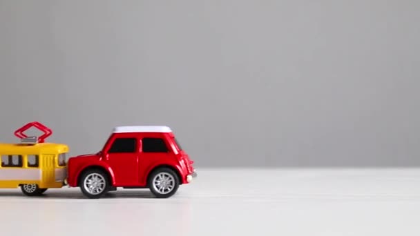 Frontalkollision mellan motorfordon och kollektivtrafik. Gul spårvagn leksak modell och röd auto leksak kollision på en vit bakgrund — Stockvideo