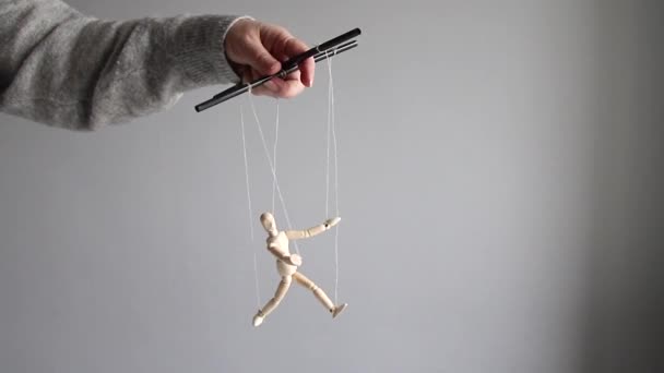 Manipulator kobieca ręka manipuluje drewnianą lalką na szarym tle. — Wideo stockowe