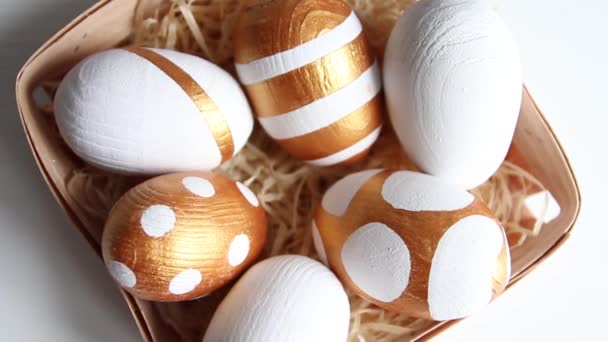 Huevos de Pascua decorados en una canasta de madera con heno sobre una mesa blanca. Vista desde arriba. Feliz concepto de Pascua . — Vídeos de Stock