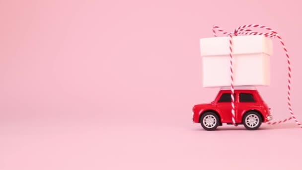 Piros játék autó szállítási ajándék doboz szalaggal íj rózsaszín háttér. Születésnap, Valentin-nap, Nők napja koncepció.