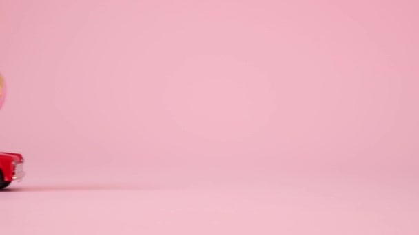 Coche modelo de juguete rojo con un huevo de patrón dorado sobre un fondo rosa. Entrega de regalos. Feliz concepto de Pascua — Vídeo de stock