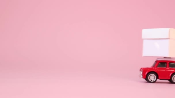 Rote kleine Spielzeugauto Lieferung Geschenkschachtel mit Schleife auf rosa Hintergrund. Geburtstag, Valentinstag, Frauentag. — Stockvideo