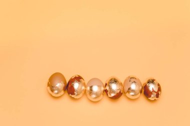 Paskalya tebrik kartı. Sıraya dizilmiş altın yumurtalar bej arka planda