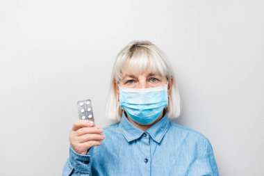 Tıbbi maske takan yetişkin bir kadının elinde haplar var.