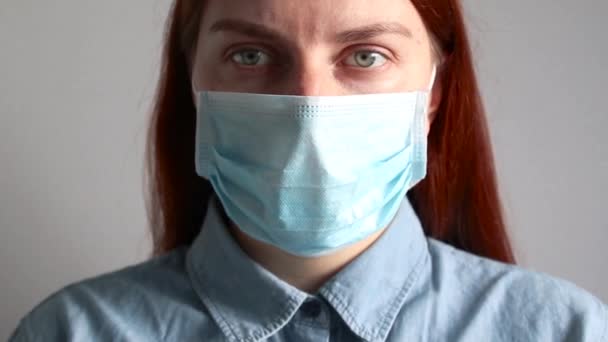 Red-haired girl in medical mask looks into the camera — ストック動画