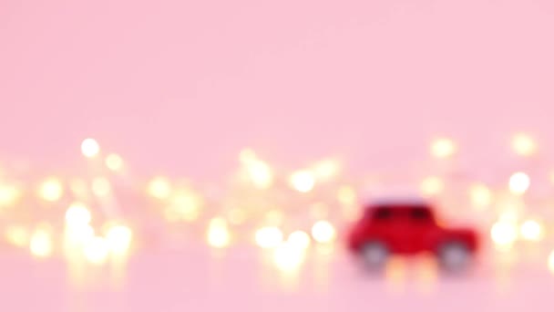 Giocattolo rosso per bambini giostre in auto e una ghirlanda d'oro lampeggiante su uno sfondo rosa. Concetto di consegna — Video Stock