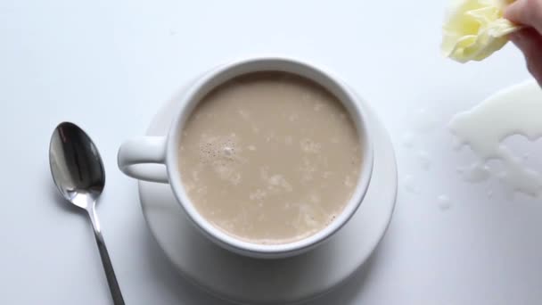 Keramik weiße Tasse Kaffee mit Milch auf einer Untertasse, ein Metalllöffel auf dem Tisch. Weibliche Hand wischt verschüttete Milch mit Serviette ab. — Stockvideo