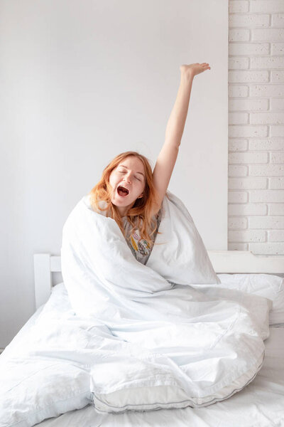 Blonde woman while stretching on bed after waking up. Vertical photo