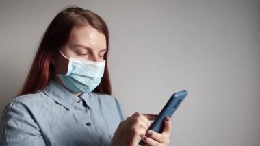Tıbbi maskeli genç bir kadın haberlere akıllı telefondan bakıyor.