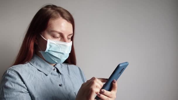 Jonge vrouw met medisch masker kijkt door de nieuwsfeed op een smartphone — Stockvideo