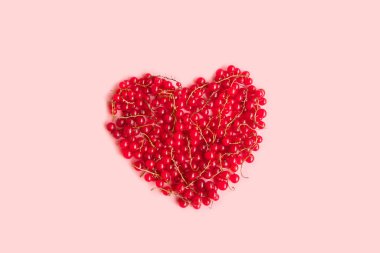 Pembe arka planda kalp şeklinde taze kırmızı bektaşi üzümü.
