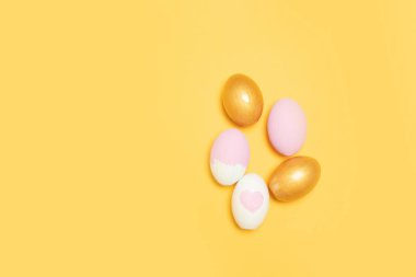 Sarı arka planda altın ve pembe paskalya yumurtalarının üst görüntüsü