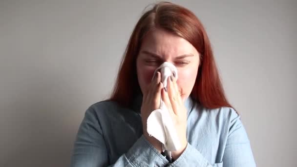 Uma jovem ruiva com uma camisa azul de ganga sopra o nariz em um lenço. Conceito de vírus — Vídeo de Stock