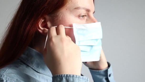Uma jovem ruiva coloca corretamente uma máscara médica em seu rosto. Proteção contra ar sujo, conceito de vírus — Vídeo de Stock