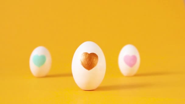 Tres huevos de Pascua blancos con el arte de la decoración del corazón sobre un fondo amarillo. Composición festiva. Amor corazón dibujo — Vídeos de Stock