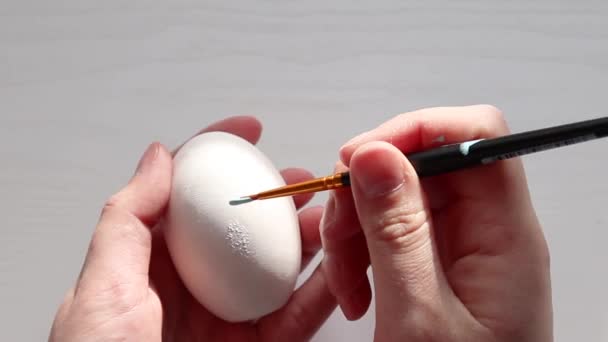 Γυναικείο χέρι ζωγραφίζει ένα λευκό αυγό κοτόπουλου με μπλε χρώμα για τις διακοπές. Έννοια Πάσχα. — Αρχείο Βίντεο