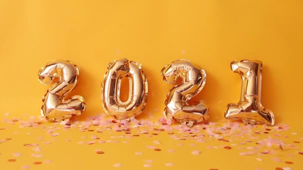 Altın 2021 numaralı helyum balonları. Sarı arka planda pembe parıltılı konfetiler.. — Stok video