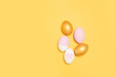 Sarı arka planda altın ve pembe paskalya yumurtalarının üst görüntüsü