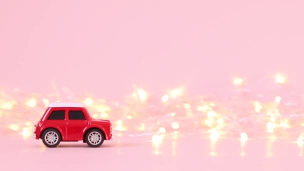 Красная игрушечная машина для детей и золотая гирлянда на розовом фоне. Концепция праздника — стоковое видео