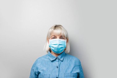 Mavi gömlekli yetişkin sarışın kadın tek kullanımlık tıbbi maske takıyor. Roman Coronavirus, 2019-NCoV koruması