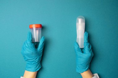 Doctor hands in latex rubber gloves holding a plastic container and a lubricant of liquids on blue background clipart