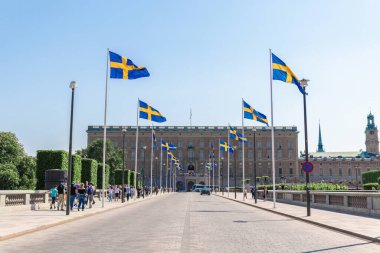 Sokak otoyolu boyunca metal direkler üzerinde İsveç bayrakları. Turistler güneşli bir günde yürürler.